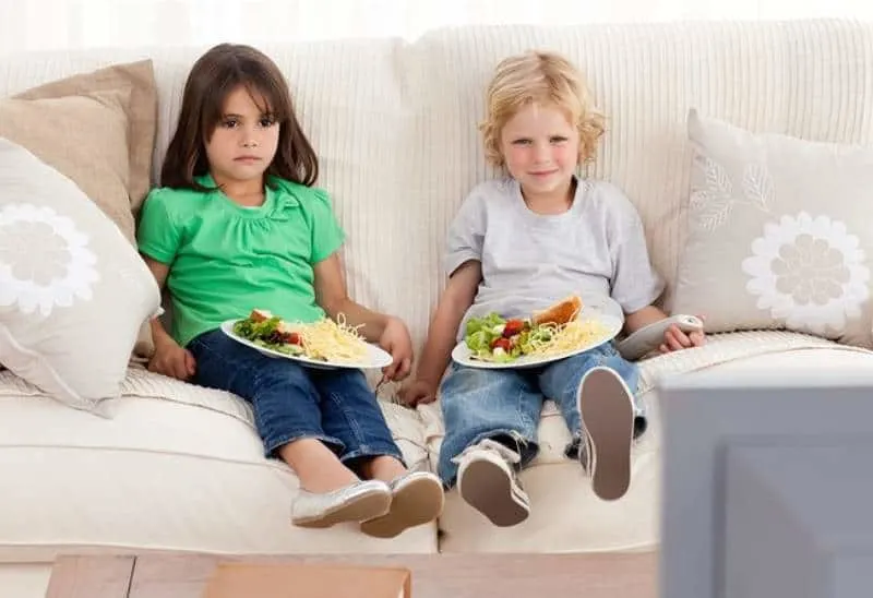 two children sitting on couch and watching a tv