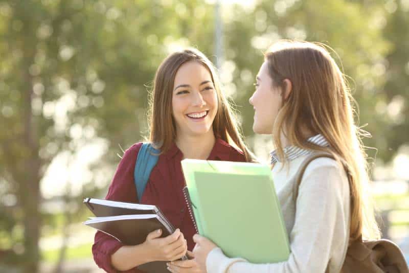 dos estudiantes sonrientes caminando y hablando en un campus