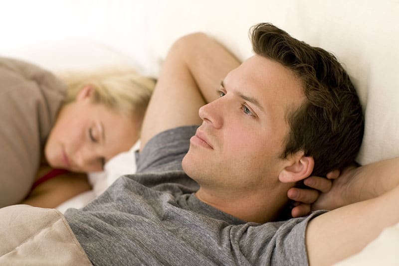 worried man in deep thoughts while woman sleeping