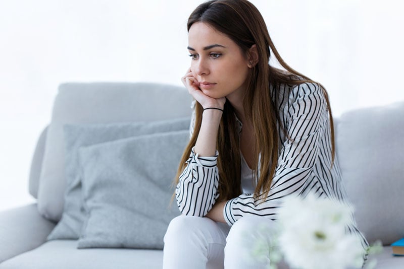 worried woman sitting on the couch in deep thoughts
