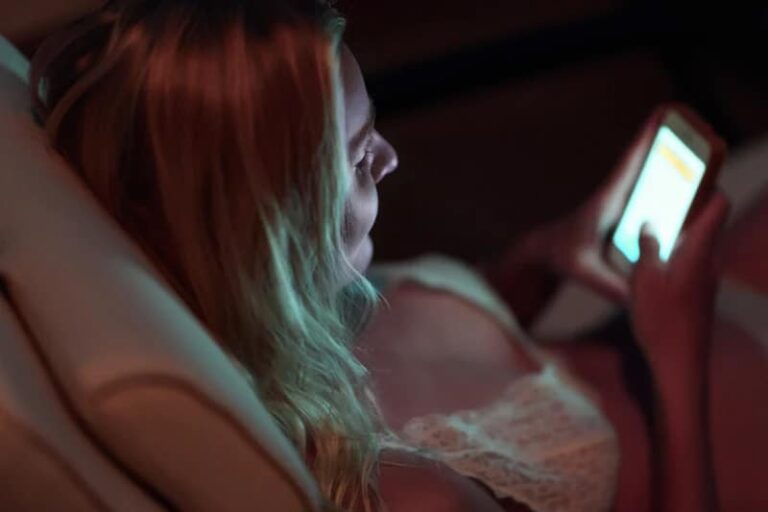 high angle of woman typing on her phone while lying on bed