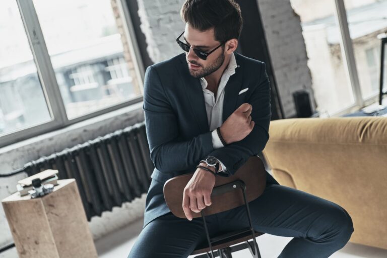 a handsome man in a suit sitting on a chair in an apartment