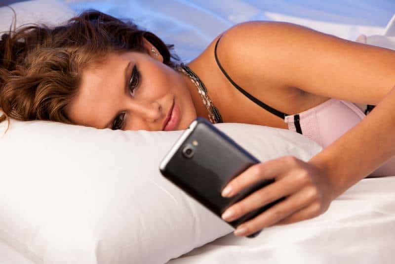 Donna assonnata che controlla i messaggi sul cellulare