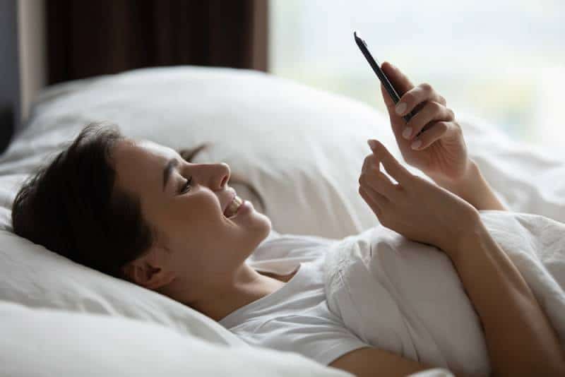 Joven sonriente tumbada en cama blanca