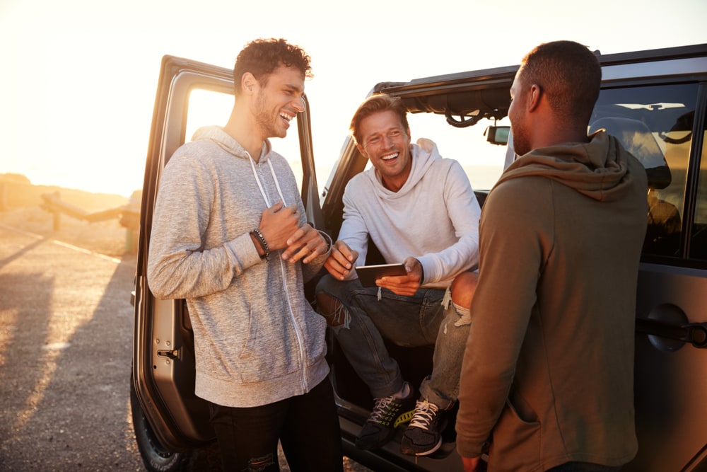 a man with friends is standing next to a car