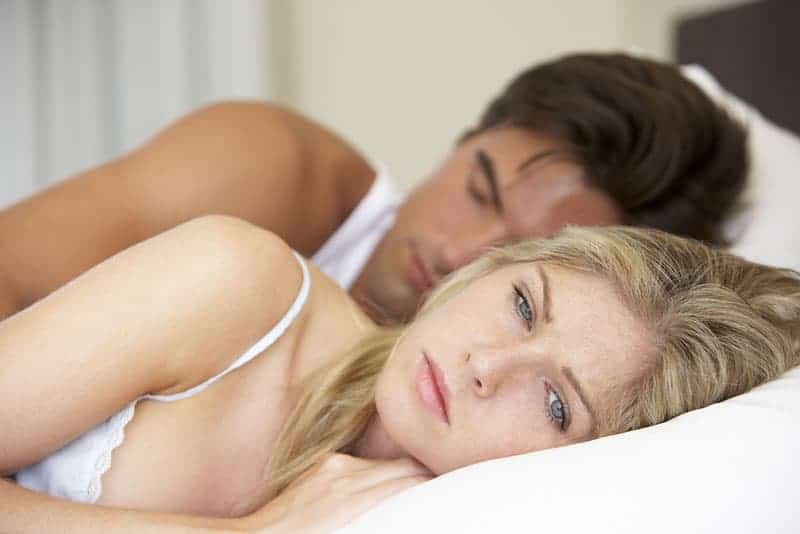 mujer rubia preocupada tumbada en la cama junto a su novio