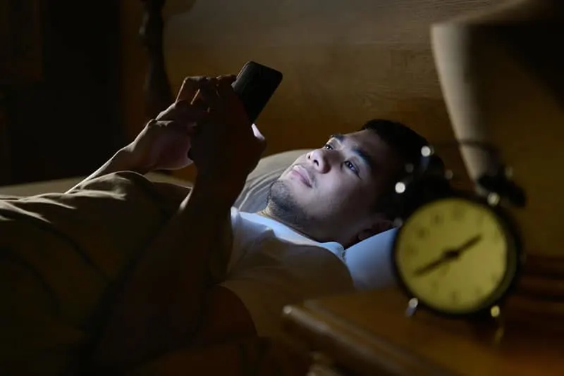 man lying on bed and typing on his phone