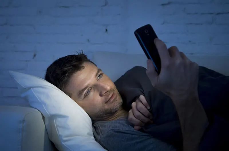 man lying on couch and typing on his phone
