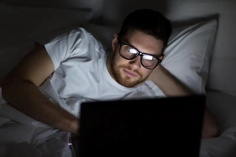 man wearing eyeglasses typing on his laptop before sleep