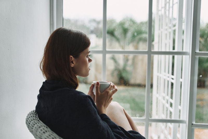 Una donna pensierosa che beve un caffè vicino alla finestra