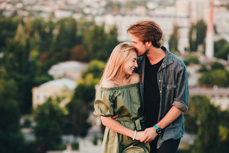 pareja sonriente hombre besa a mujer en la frente al aire libre