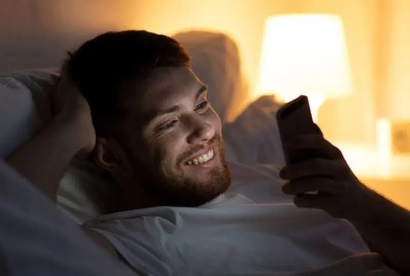 smiling man typing on his phone at night