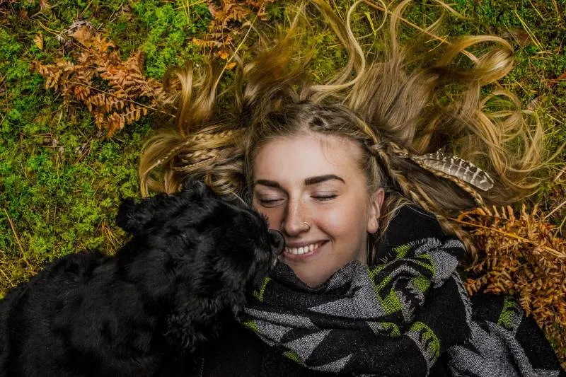 smiling woman lying on the ground next to black dog during the day