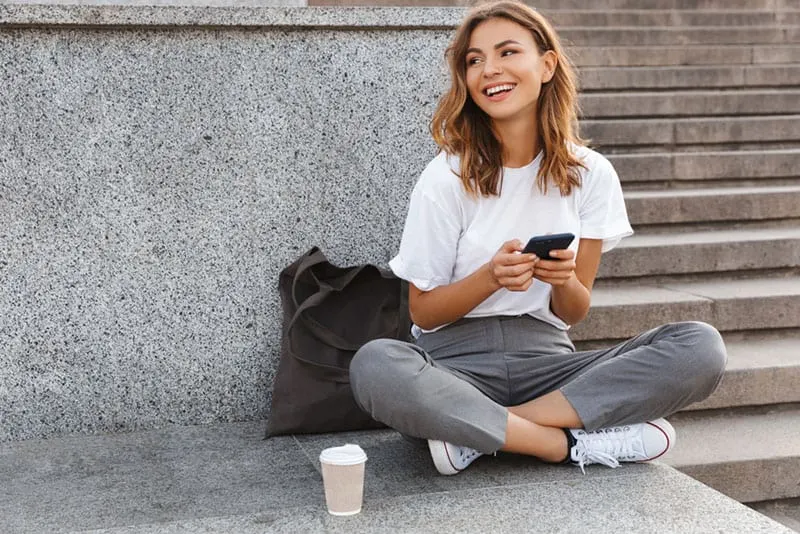 smiling woman texting while sitting outdoor on the floor
