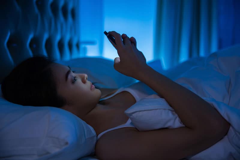 donna che scrive sul suo telefono mentre è sdraiata sul letto durante la notte