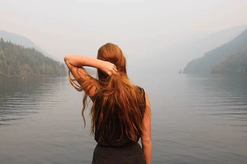 woman with red hair standing by the lake