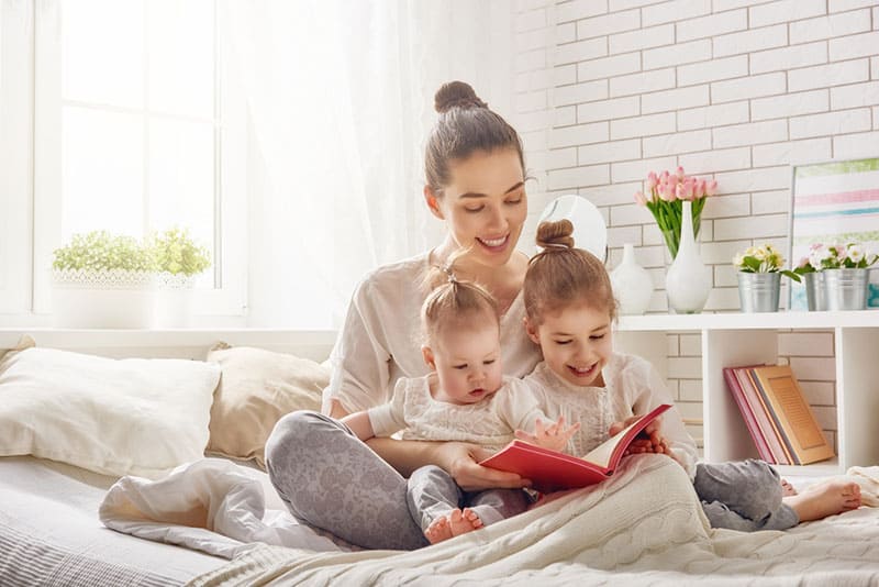 young mother reading a book to her daughters