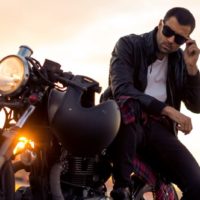un uomo affascinante con una giacca di pelle nera e occhiali da sole reyban siede su una moto