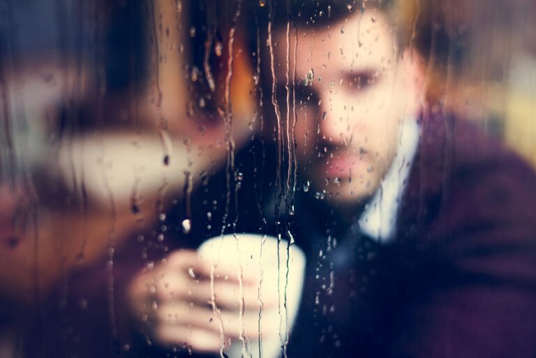a sad man behind wet glass