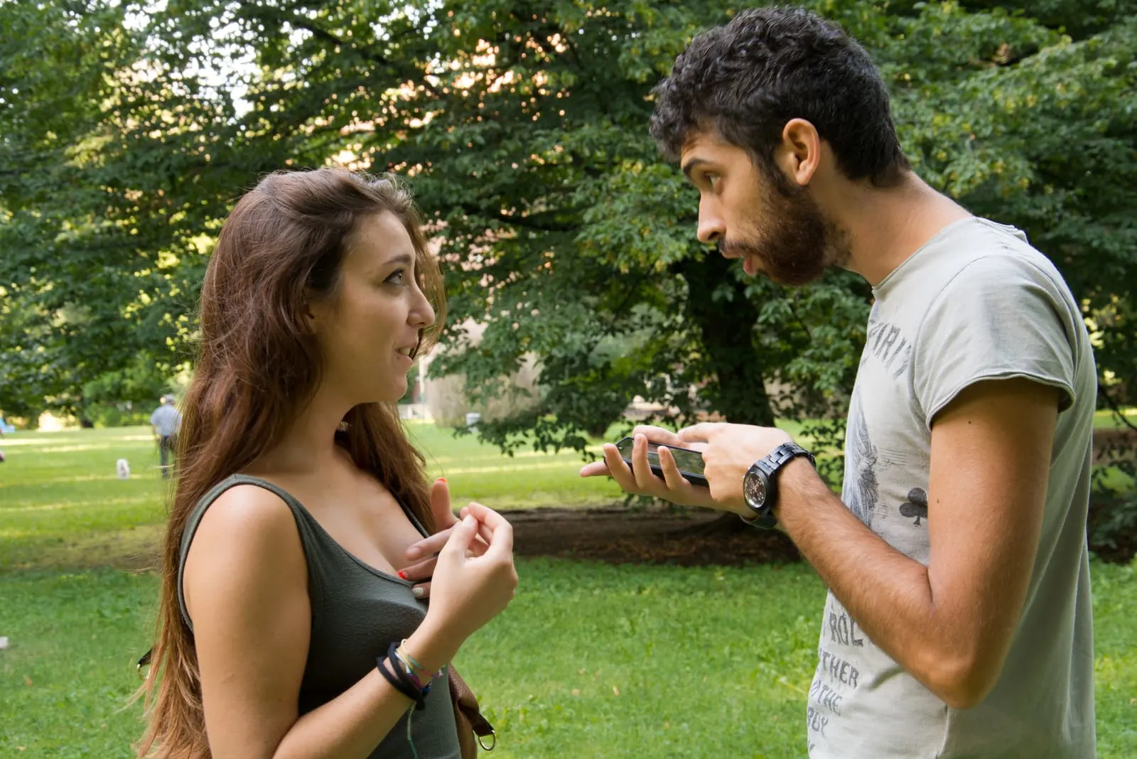 a jealous man with a cell phone in his hand in a park is arguing with a girl