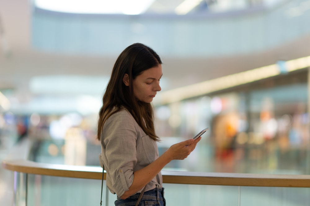 a sad brunette in a shopping mall uses a smartphone