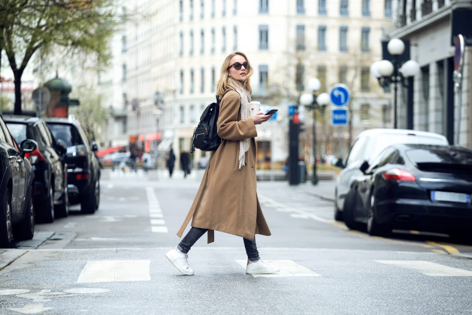 a woman in a brown coat with a phone in her hand walks down the street