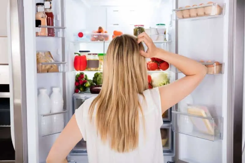 back view of confused woman standing in front of fridge