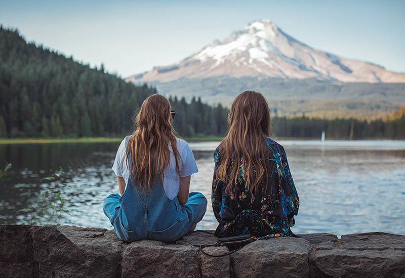 vista trasera de dos amigas sentadas frente al agua