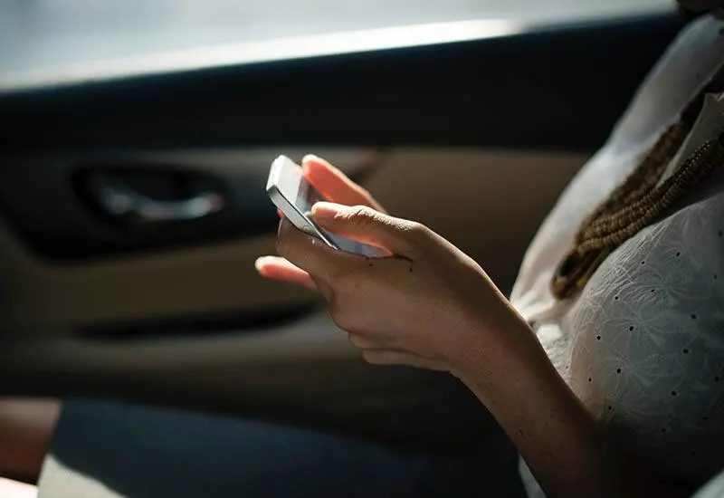 close up photo of woman typing a on her phone in car