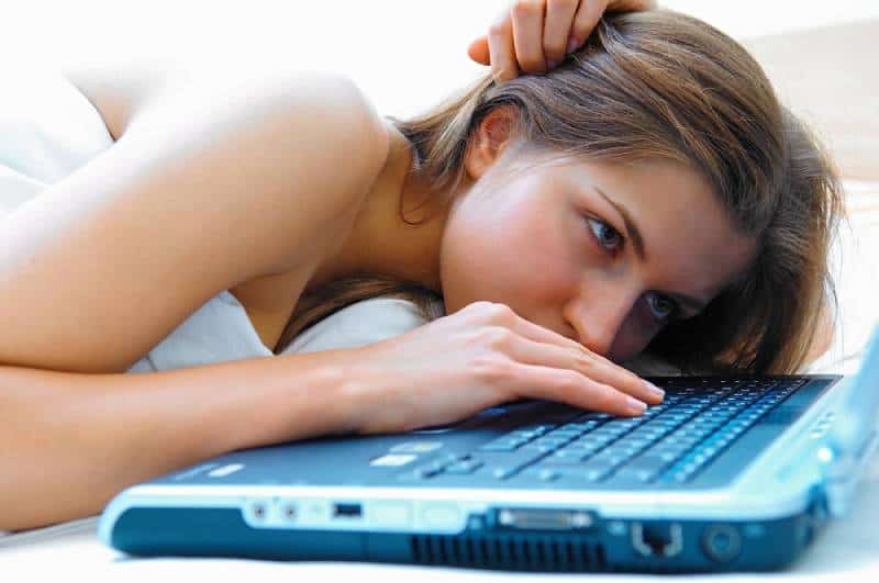 girl lying in bed and typing on laptop