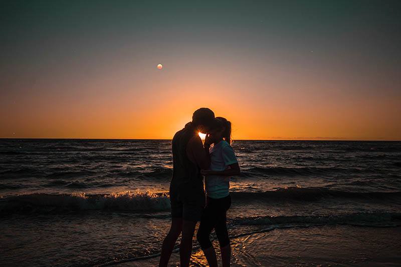 man kissing a woman at sunset