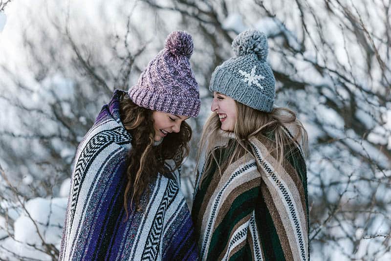 two smiling female friends covered with blanket during winter time