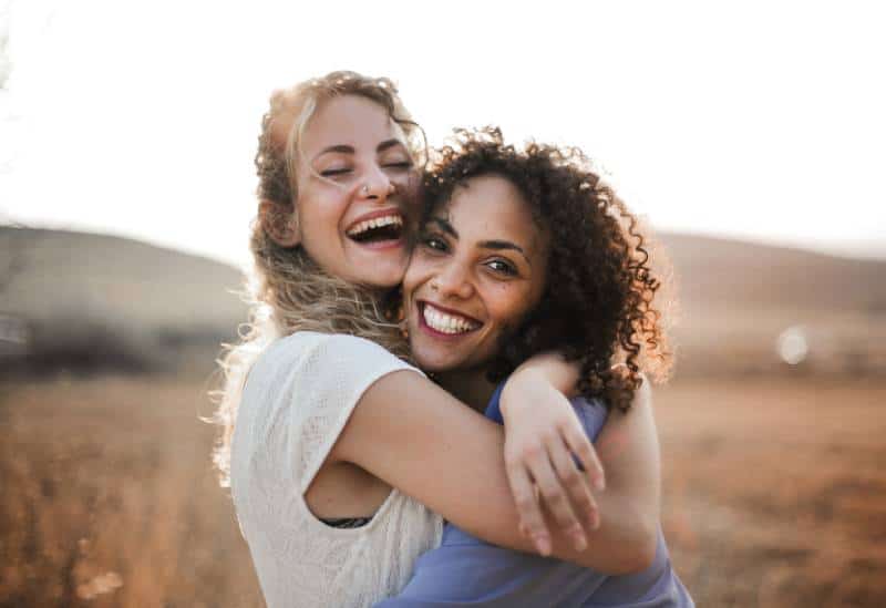 two smiling female friends hugging each other outside