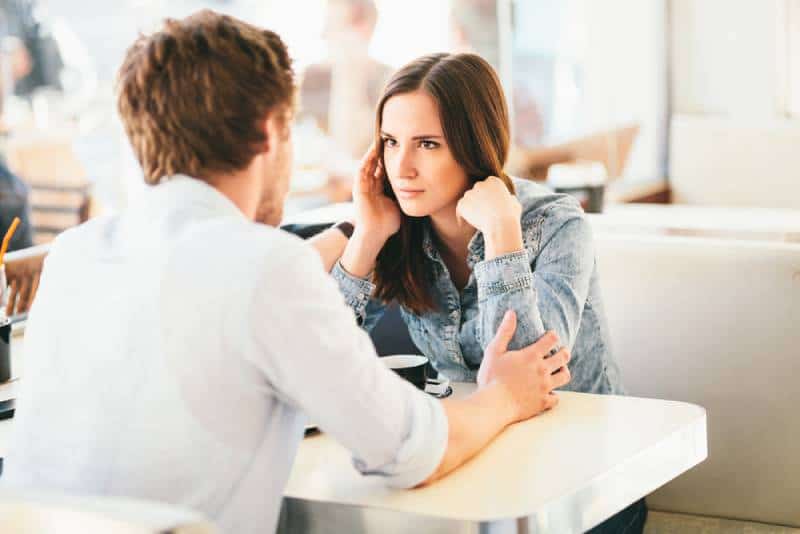 woman suspiciously looking at man while he holding her arms in cafe