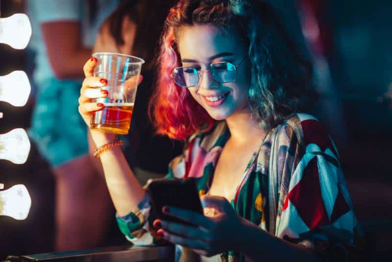 young woman drinking beer and typing on her smartphone