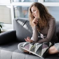 depressed woman sitting on sofa with pillow on knee
