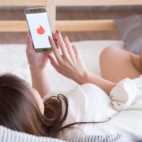 woman lying in bed and looking tinder application