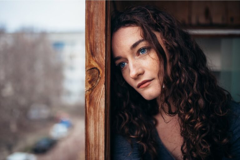 sad woman standing by the balcony door