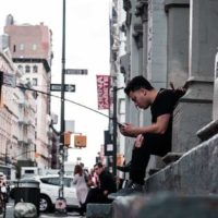 hombre sentado en las escaleras de hormigón en la calle y escribiendo en su teléfono