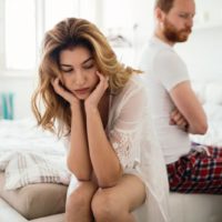 sad woman sitting next to man on the bed