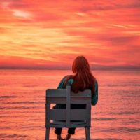 mulher sentada numa cadeira em frente ao mar durante o pôr do sol
