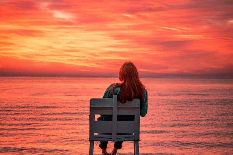 woman sitting on chair in front of sea during sunset