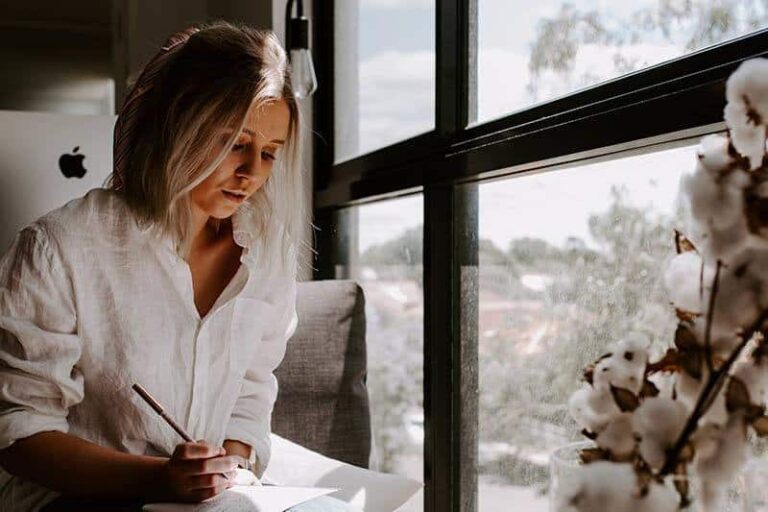 woman writing a letter beside window at home