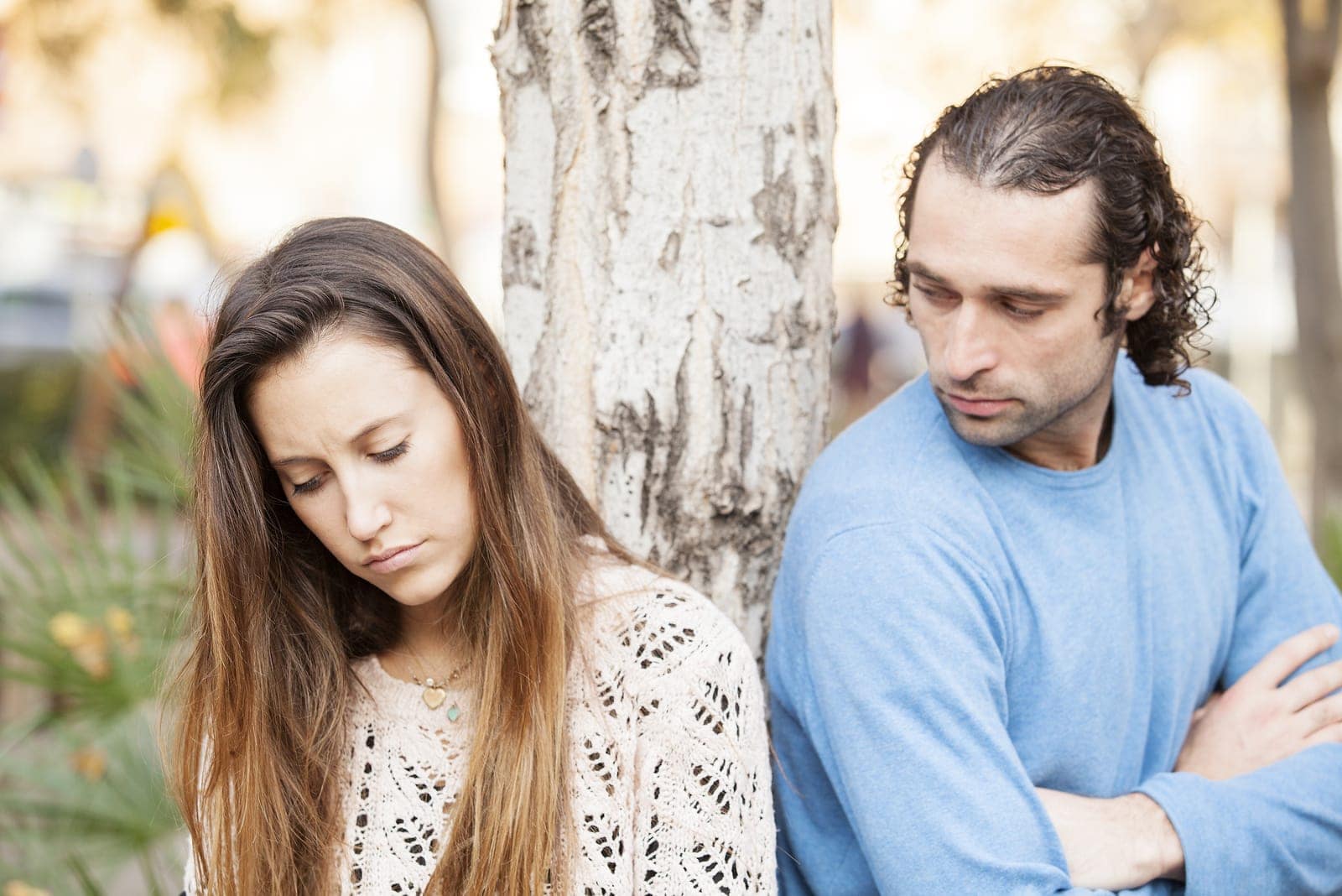 a sad loving couple standing outside by a tree