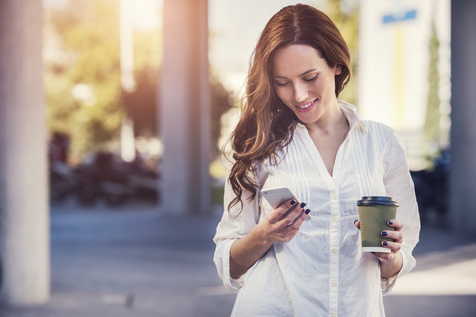 hermosa morena sonriente de pie fuera y utiliza su teléfono móvil