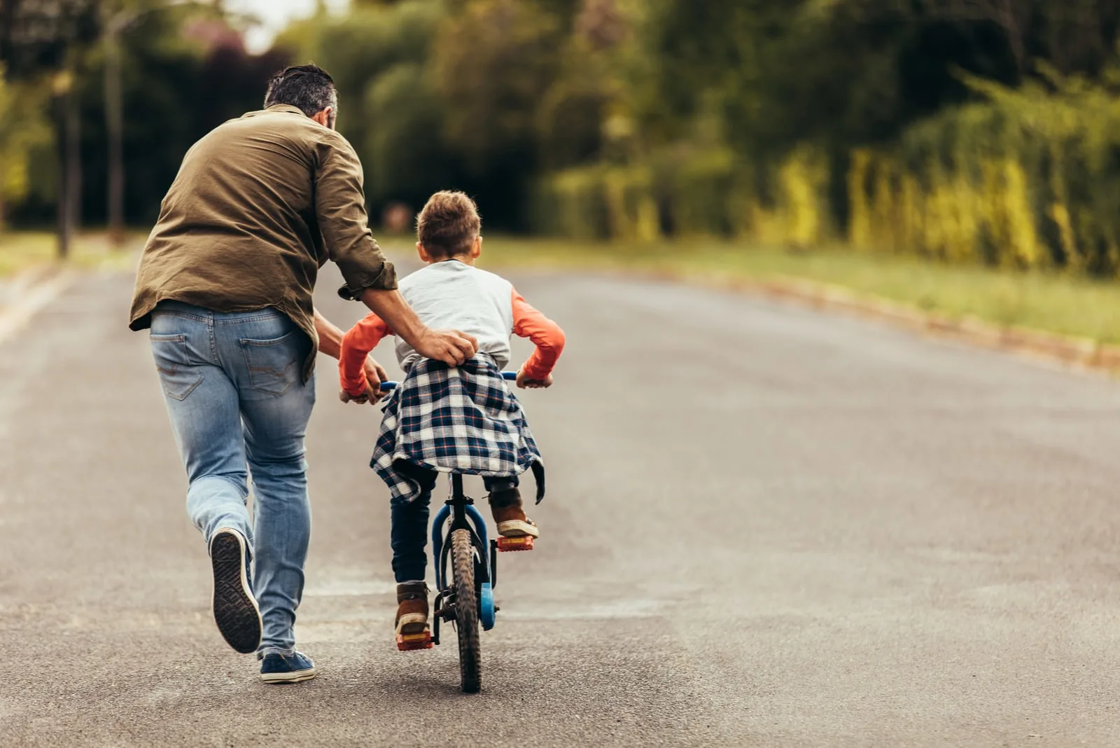 boy riding a bicycle while his father runs along holding the kid