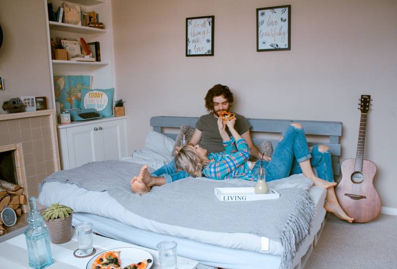 homem e mulher deitados na cama e a comer pizza