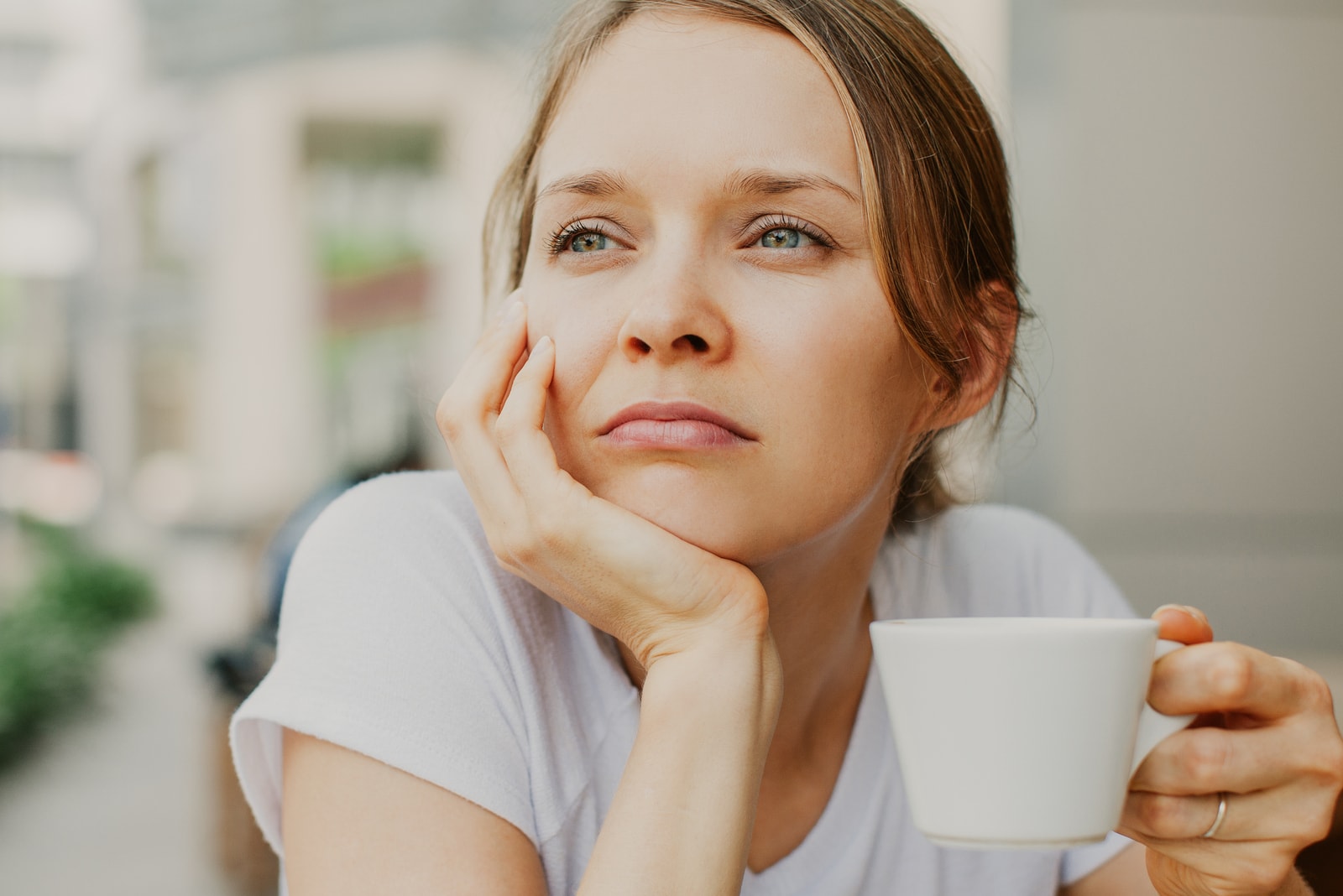 mujer hermosa joven pensativa que bebe el café al aire libre