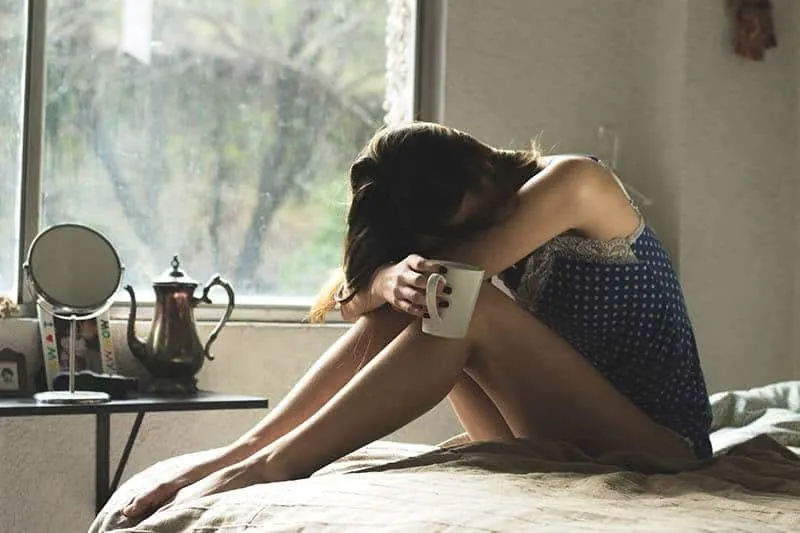 sad woman sitting on the bed holding a cup