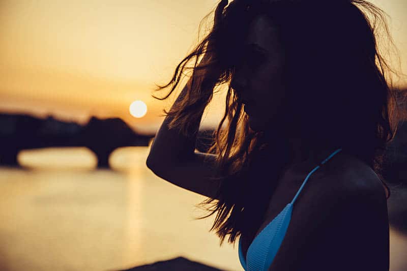 side view of shallow focus of woman in bikini standing by the water during golden hour